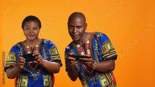 Ethnic couple having fun with mobile videogames on phone, participating in online gaming tournament on camera. African american man and woman playing in game contest on smartphone.