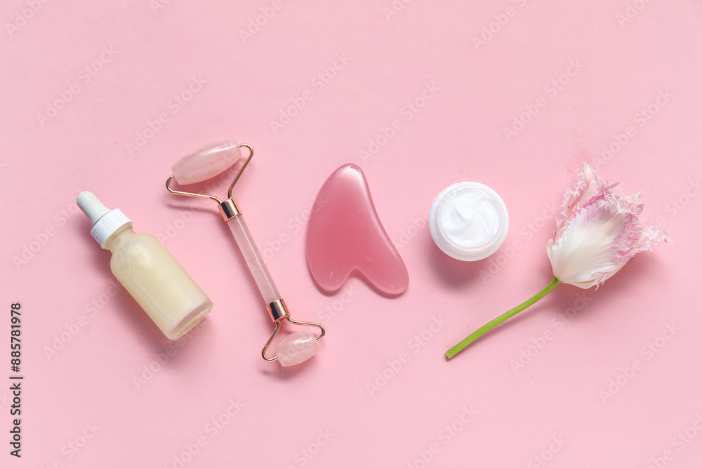 Jade roller with gua sha, serum, cosmetic cream and tulip flower on pink background Jade roller with gua sha, serum, cosmetic cream and tulip flower on pink background