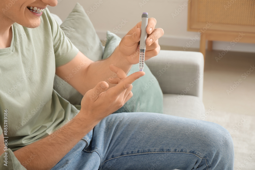 Diabetic young man using lancet pen on sofa at home, closeup Diabetic young man using lancet pen on sofa at home, closeup