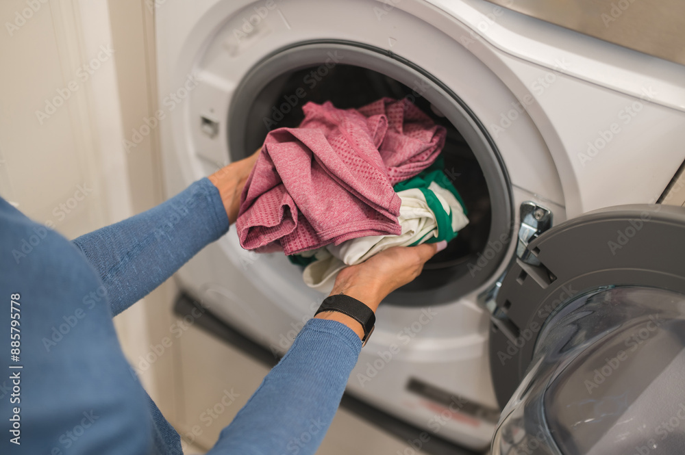 Woman putting clothes into the washing machine for washing Woman putting clothes into the washing machine for washing