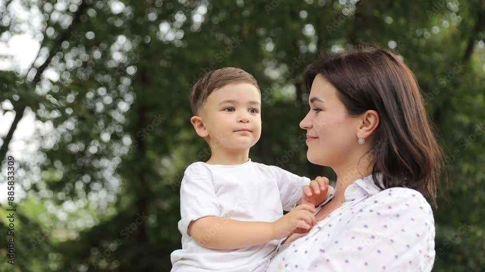 Young mother holding her son, they walking together in summer park Young mother holding her son, they walking together in summer park