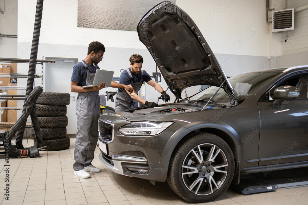 Two auto mechanics inspecting car engine in workshop environment. Professionals diagnosing vehicle with laptop and tools. Automotive maintenance, repair, and teamwork concept Two auto mechanics inspecting car engine in workshop environment. Professionals diagnosing vehicle with laptop and tools. Automotive maintenance, repair, and teamwork concept