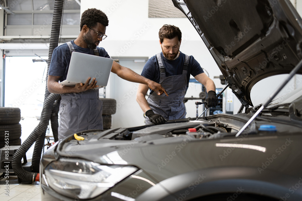 Auto mechanics working on car in garage using laptop for diagnostics. Collaboration, teamwork, and expert car maintenance are highlighted as they engage in repair and service procedures. Auto mechanics working on car in garage using laptop for diagnostics. Collaboration, teamwork, and expert car maintenance are highlighted as they engage in repair and service procedures.