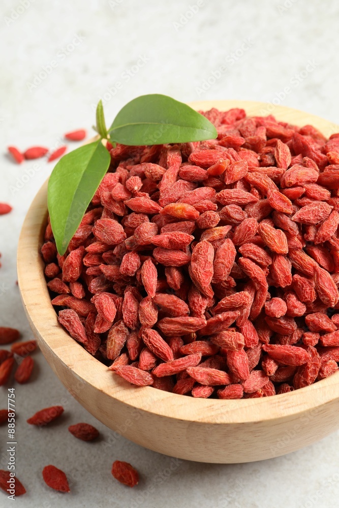 Dried goji berries and leaves in bowl on light textured table, closeup Dried goji berries and leaves in bowl on light textured table, closeup