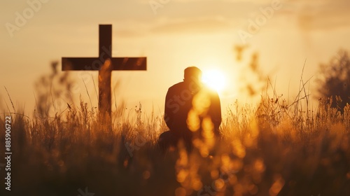 A silhouette of a man kneeling in the middle of a peaceful meadow at sunrise. Man praying at the foot of the cross at sunrise.
