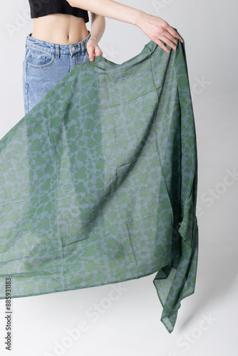 Model girl holding big green spring scarf in hands and posing on a white background. Fit woman wearing light blue jeans photo