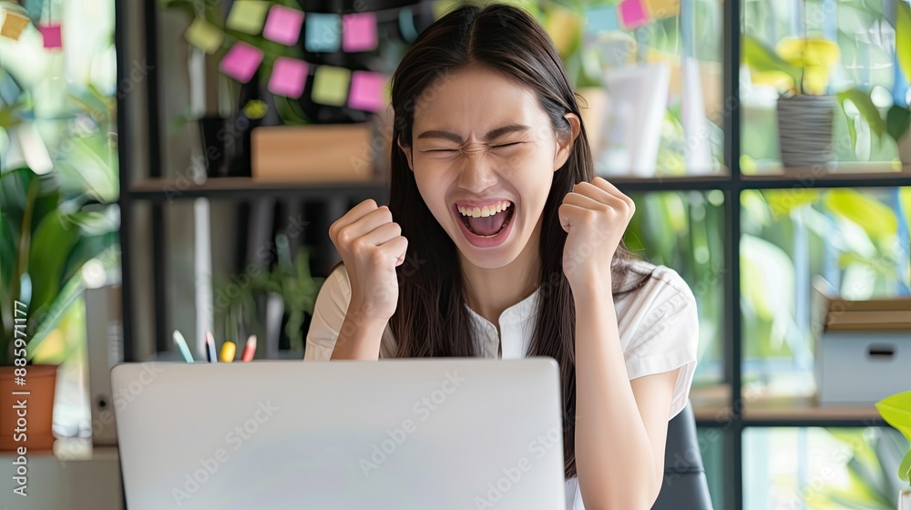 Fototapeta premium Joyful Asian executive in office, excitedly looking at laptop, celebrating good online results