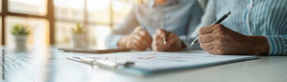 Two professionals reviewing documents and taking notes in a bright office setting, focusing on collaboration and paperwork completion. Two professionals reviewing documents and taking notes in a bright office setting, focusing on collaboration and paperwork completion.