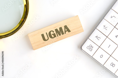 Business concept. UGMA word on wooden blocks in a composition with a magnifying glass and a calculator photo