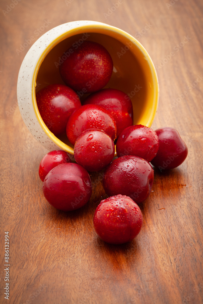 Front view of fresh Cherry Plum (Prunus cerasifera) fruits spilled out from a ceramic bowl on a wooden background. Front view of fresh Cherry Plum (Prunus cerasifera) fruits spilled out from a ceramic bowl on a wooden background.