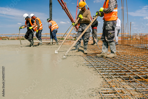 Workers in rubber boots are pouring fresh concrete in building foundation
