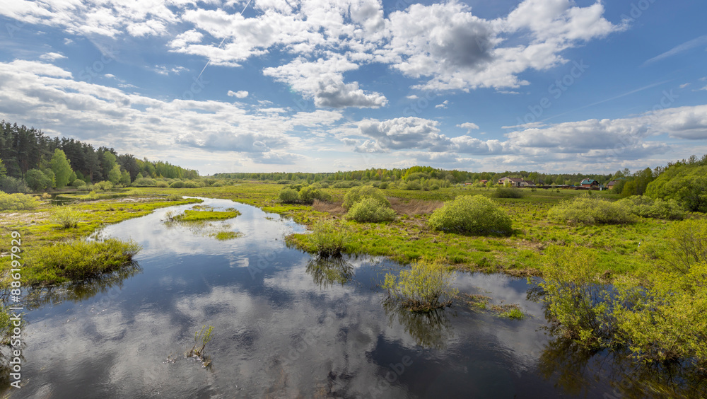 A winding river flows through a lush, green meadow under a blue sky dotted with fluffy white clouds. A winding river flows through a lush, green meadow under a blue sky dotted with fluffy white clouds.