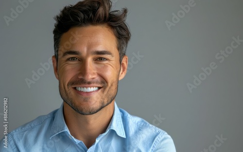 A young man with brown hair smiles brightly, wearing a white t-shirt against a blue background © imagineRbc