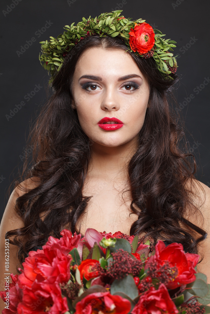 Naklejka premium Charming young woman with floral head wreath looking at camera while standing against black background