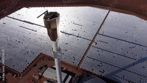 Drone shot of a solar thermal energy farm with thousands of mirrors reflecting sunlight onto a central tower where it's converted into heat and used to generate electricity photo