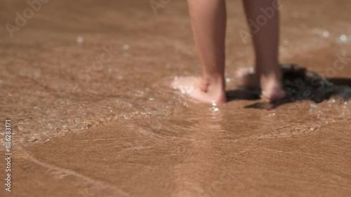 Close up funny happy child legs playing with waves on sand beach near sea. Barefoot kids feet on ocean shore at sunset. Summer vacation, holiday. family trip with kids. Tourism to warm countries. 4K.
