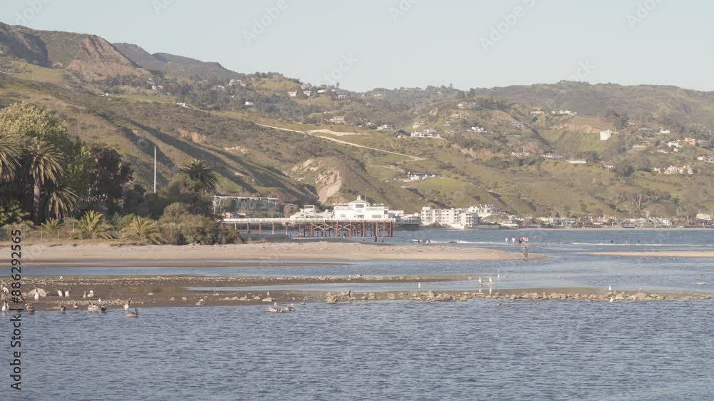 Malibu Pier Backdropped By Luxury Villas And Hills In California, USA. Malibu Lagoon In Foreground. wide static shot Malibu Pier Backdropped By Luxury Villas And Hills In California, USA. Malibu Lagoon In Foreground. wide static shot