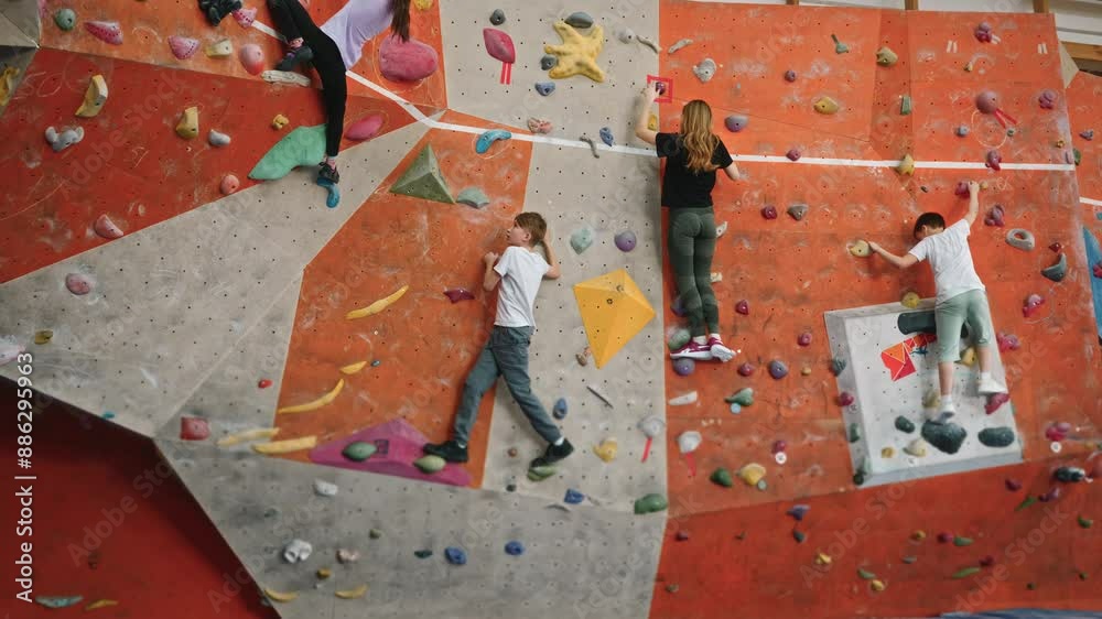 Boys and girls of 10 years old train on the indoor climbing wall. Brave children are not afraid of heights and climb a vertical wall. Team spirit in mountaineering. High quality 4k footage