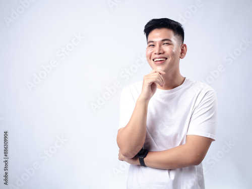 A young Asian man, wearing a white shirt and black watch, looks pensively to the side while resting his chin on his hand. The plain white background emphasizes the subject's contemplative