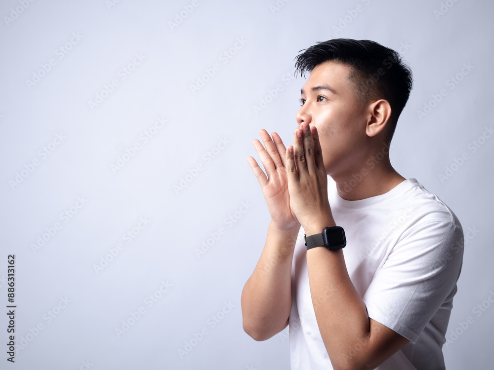 A young Asian man, wearing a white shirt and black watch, smiles widely and raises his hands near his face in an expressive and joyful manner. The plain white background highlights the subject's A young Asian man, wearing a white shirt and black watch, smiles widely and raises his hands near his face in an expressive and joyful manner. The plain white background highlights the subject's