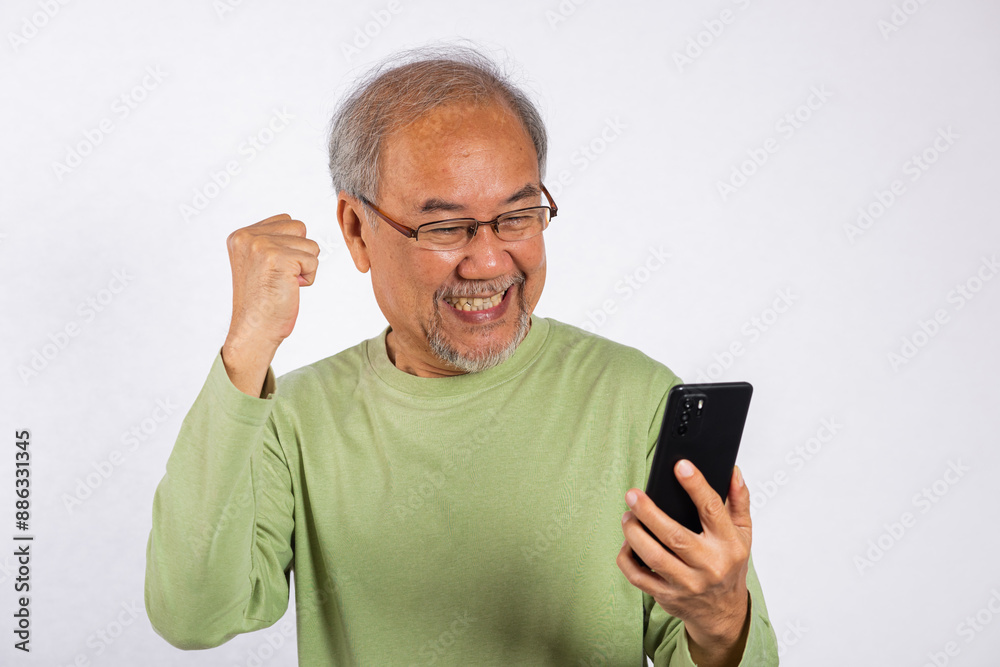 Portrait Asian smiling old man holding a cell phone celebrating something on the phone studio shot isolated on white background, happy senior man doing winner gesture celebrate on mobile phone Portrait Asian smiling old man holding a cell phone celebrating something on the phone studio shot isolated on white background, happy senior man doing winner gesture celebrate on mobile phone