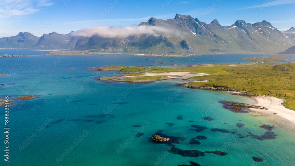 A secluded sandy beach on a Norwegian island with rocky outcroppings and lush vegetation. Turquoise waters lead to mountains cloaked in clouds. Kolbeinsanden Beach, Lofoten A secluded sandy beach on a Norwegian island with rocky outcroppings and lush vegetation. Turquoise waters lead to mountains cloaked in clouds. Kolbeinsanden Beach, Lofoten