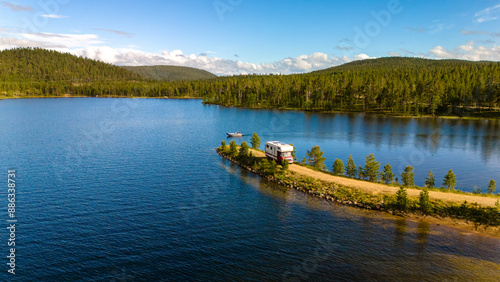 Fototapeta Naklejka Na Ścianę i Meble -  A motorhome is parked on a narrow peninsula jutting out into a serene Finnish lake, surrounded by lush green forests.