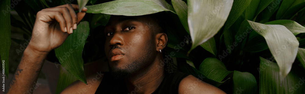 Obraz premium A stylish African American man in a black shirt holds a lush green plant in a vivid green garden.