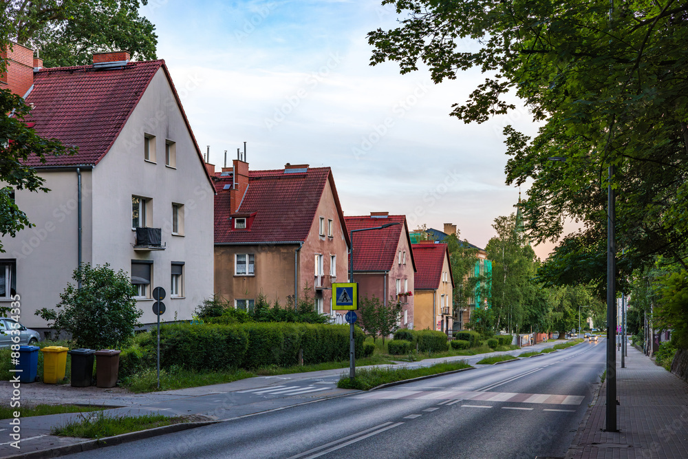 Beautiful, three-story houses with red roofs, surrounded by greenery, stand along the road. Beautiful, three-story houses with red roofs, surrounded by greenery, stand along the road.