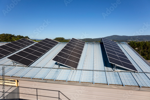 This image portrays several solar panels installed on the blue metal roof of a building, set against a clear, blue sky and distant hills in the background, emphasizing renewable energy. photo