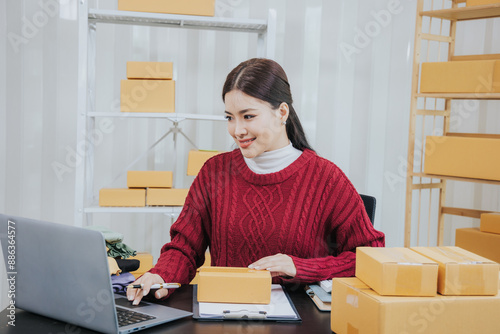 Young Asian entrepreneur running an online business from home Manage online orders and shipping packages She markets the product. Manage inventory and delight customers using laptops and smartphones. © Witoon