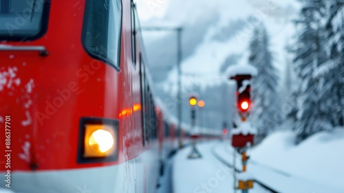 A close-up view of a red train in the snowy mountains, signaling a stop with glowing lights. Snow-covered trees and mountains surround the scene adding to its charm.