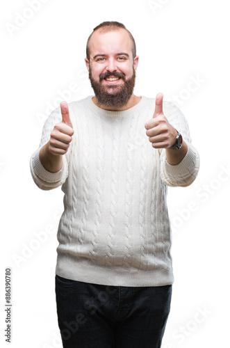 Young caucasian hipster man wearing winter sweater over isolated background approving doing positive gesture with hand, thumbs up smiling and happy for success. Looking at the camera, winner gesture.