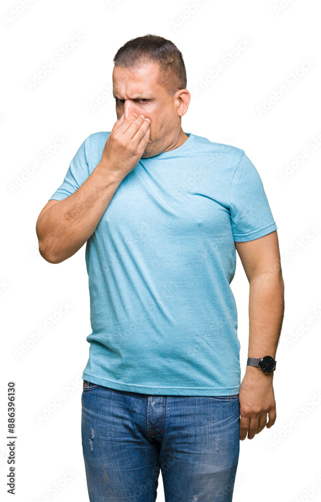 Middle age arab man wearing blue t-shirt over isolated background smelling something stinky and disgusting, intolerable smell, holding breath with fingers on nose. Bad smells concept. Middle age arab man wearing blue t-shirt over isolated background smelling something stinky and disgusting, intolerable smell, holding breath with fingers on nose. Bad smells concept.