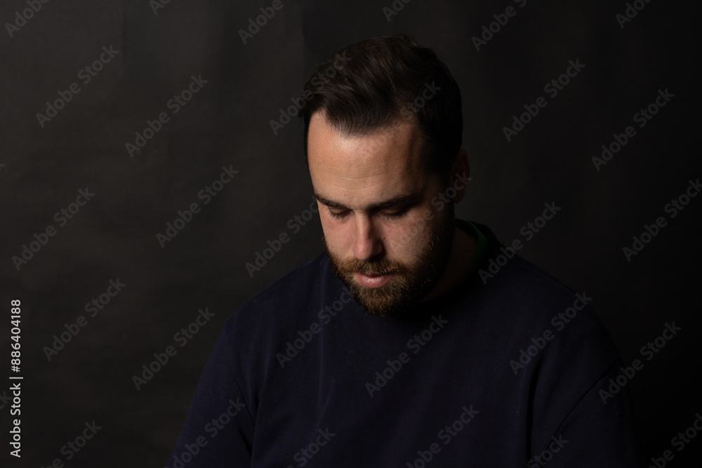 Bearded man looking down with sad expression on black background Bearded man looking down with sad expression on black background