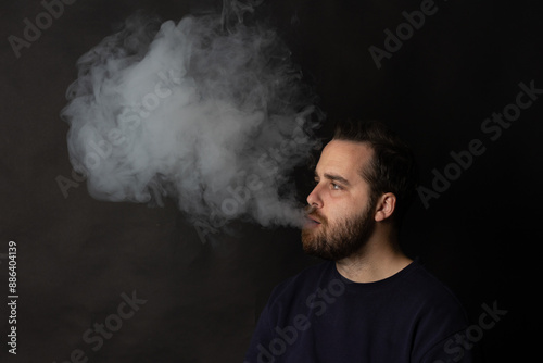 Young man smoking electronic cigarette exhaling large cloud of smoke