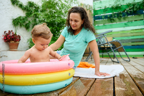 Mother watching her baby play in a colorful inflatable pool outdoors