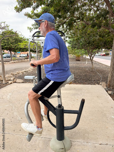 Attractive smiling retired man exercising outdoors with sports free equipment to keep fit. Cardio and muscle exercises for mature people. Athletic spirit concept