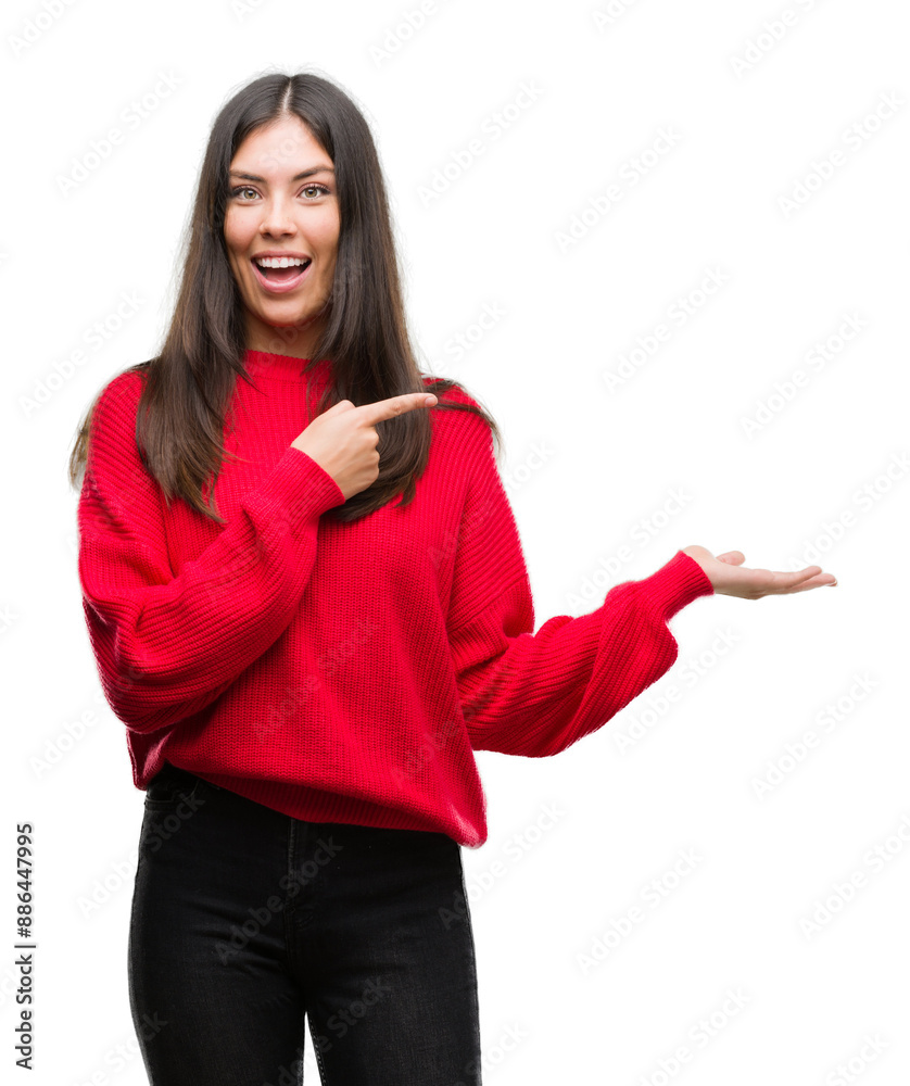 Young beautiful hispanic wearing red sweater amazed and smiling to the camera while presenting with hand and pointing with finger. Young beautiful hispanic wearing red sweater amazed and smiling to the camera while presenting with hand and pointing with finger.
