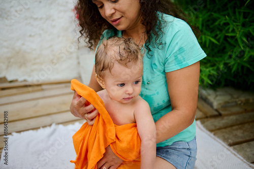 Mother drying her baby with an orange towel outdoors on a sunny day photo