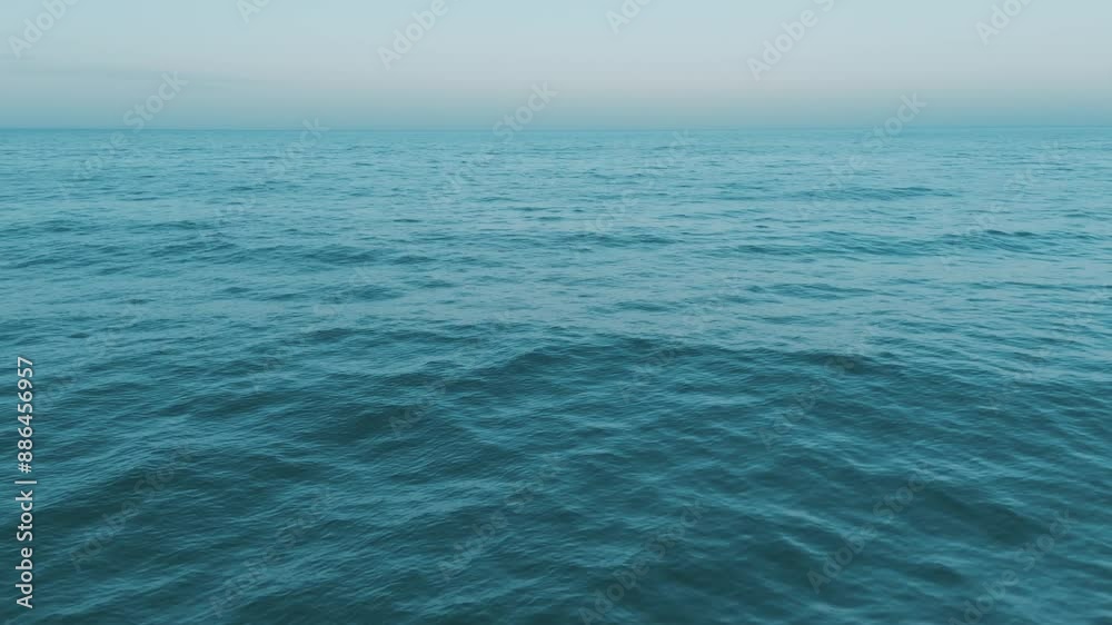 A serene view of tranquil blue ocean waves under a clear sky at sunset, creating a peaceful scene in nature