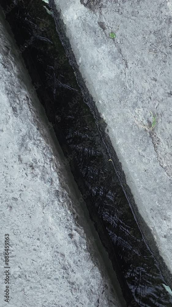 Concrete sidewalk drain with rainwater, top view.