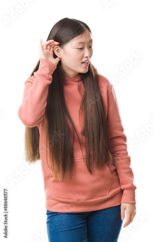 Young Chinese woman over isolated background wearing sport sweathshirt smiling with hand over ear listening an hearing to rumor or gossip. Deafness concept.