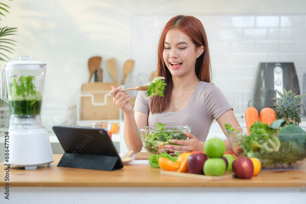 Young woman eating healthy vegetable salad and using digital tablet on the kitchen table with green fresh ingredients. Young woman eating healthy vegetable salad and using digital tablet on the kitchen table with green fresh ingredients.