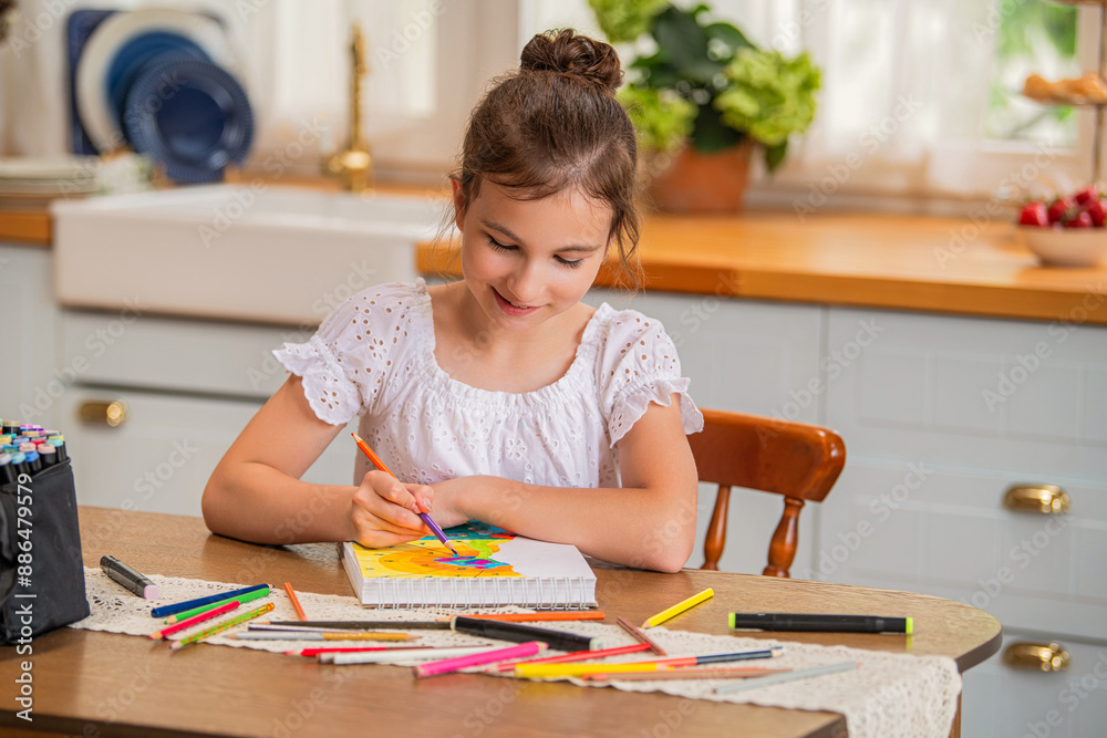 a girl draws in an album with colored pencils while sitting at a table in the interior of a country house kitchen. a girl draws in an album with colored pencils while sitting at a table in the interior of a country house kitchen.