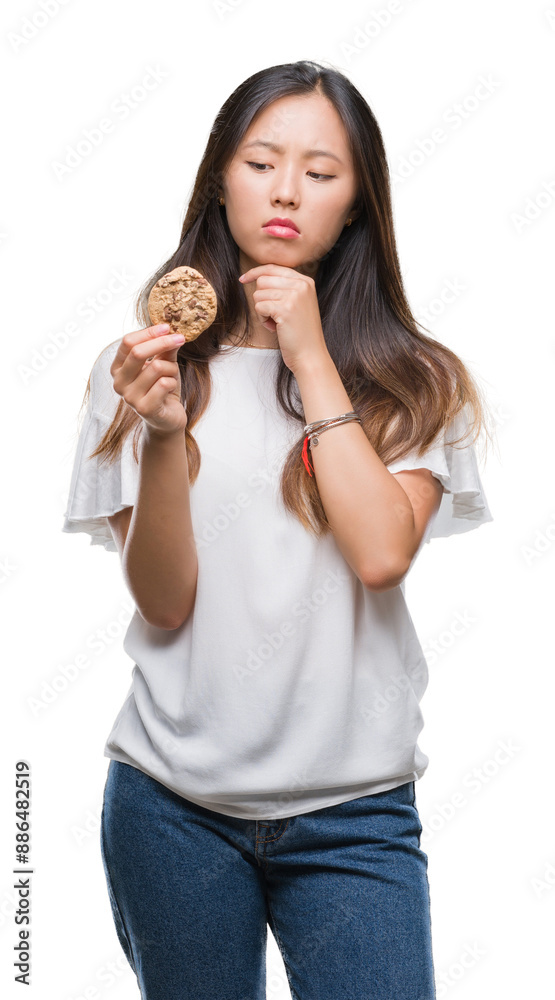 Young asian woman eating chocolate chip cookie over isolated background serious face thinking about question, very confused idea Young asian woman eating chocolate chip cookie over isolated background serious face thinking about question, very confused idea