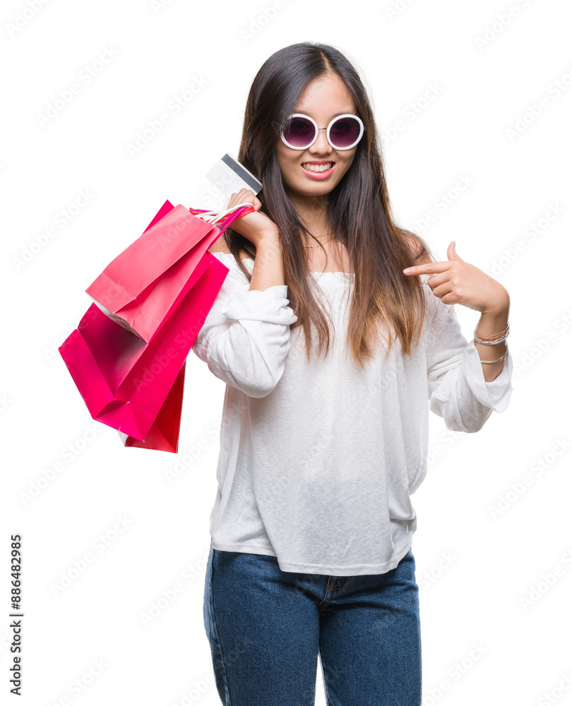 Young asian woman holding shopping bags on sales over isolated background with surprise face pointing finger to himself Young asian woman holding shopping bags on sales over isolated background with surprise face pointing finger to himself