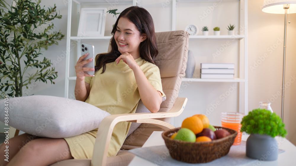 Portrait of happy young woman using mobile phone while relaxing in the armchair at cozy home. Portrait of happy young woman using mobile phone while relaxing in the armchair at cozy home.