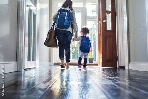 Mother holding her daughter's hand as they are leaving home, both carrying backpacks photo