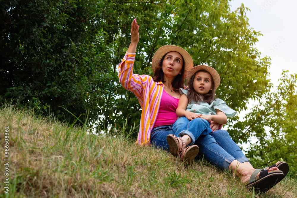 Woman mother tells an interesting story to her little daughter while sitting together in a park under a tree. Happy moments spent with your child. Woman mother tells an interesting story to her little daughter while sitting together in a park under a tree. Happy moments spent with your child.
